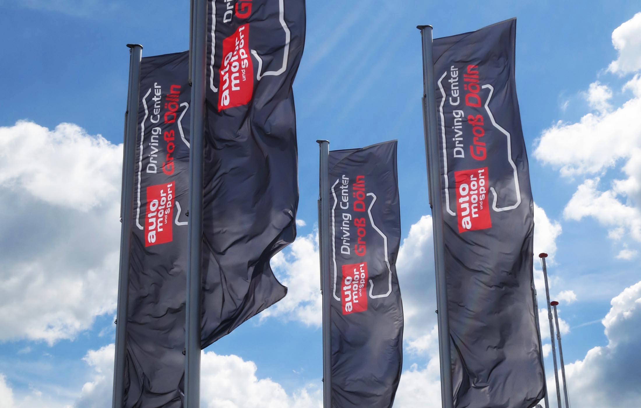 Hohe schwarze Fahnen mit der Aufschrift „Driving Center Groß Dölln“ und „auto motor und sport“ wehen im Wind.