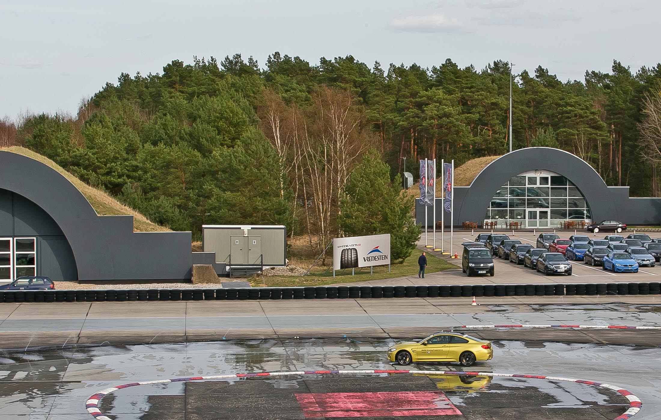 Blick auf das Driving Center Groß Dölln mit geparkten Fahrzeugen und Teststrecke im Vordergrund.
