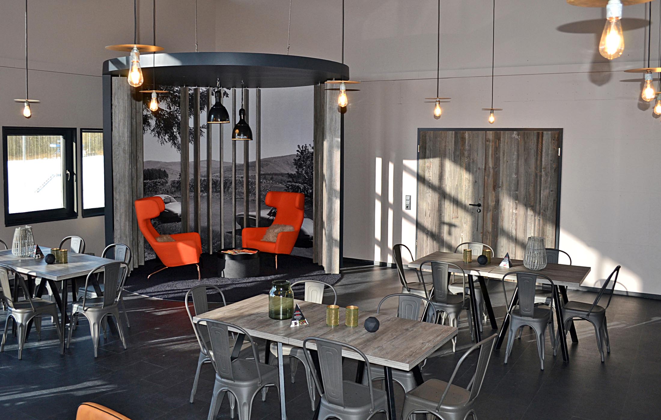 Nischenbereich mit zwei roten Sesseln vor großem Wandbild und modernen Hängelampen.