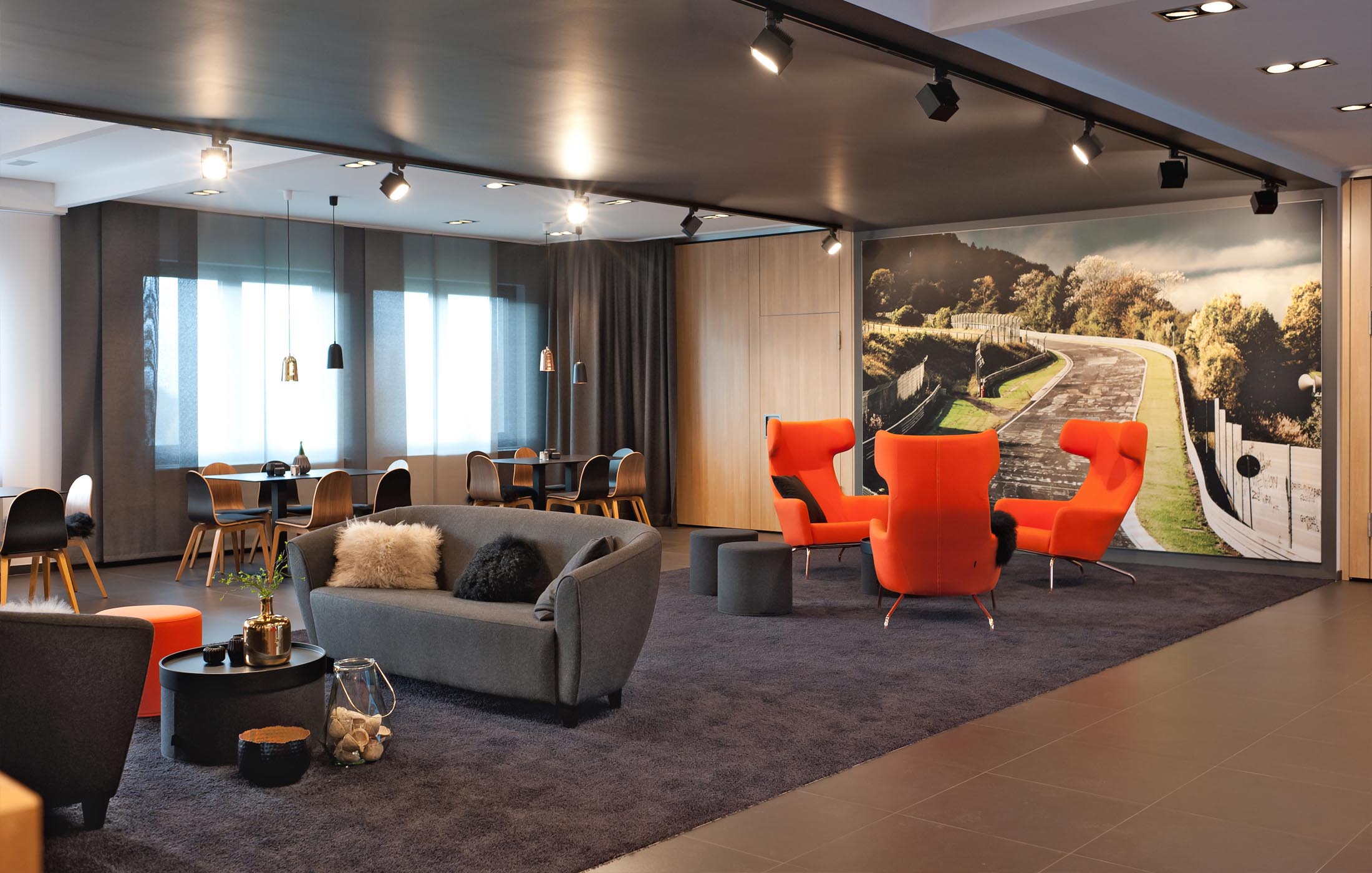 Loungebereich mit roten Sesseln und Sofa vor einer Fototapete der Nürburgring-Rennstrecke.