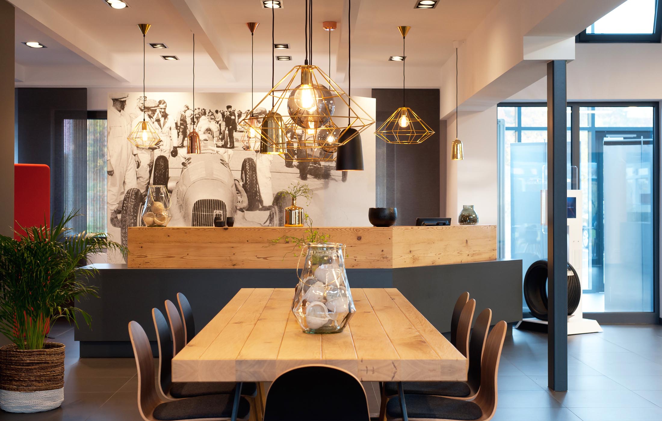 Moderner Empfangsbereich mit Holztheke, Hängelampen und großem historischen Rennsport-Foto.