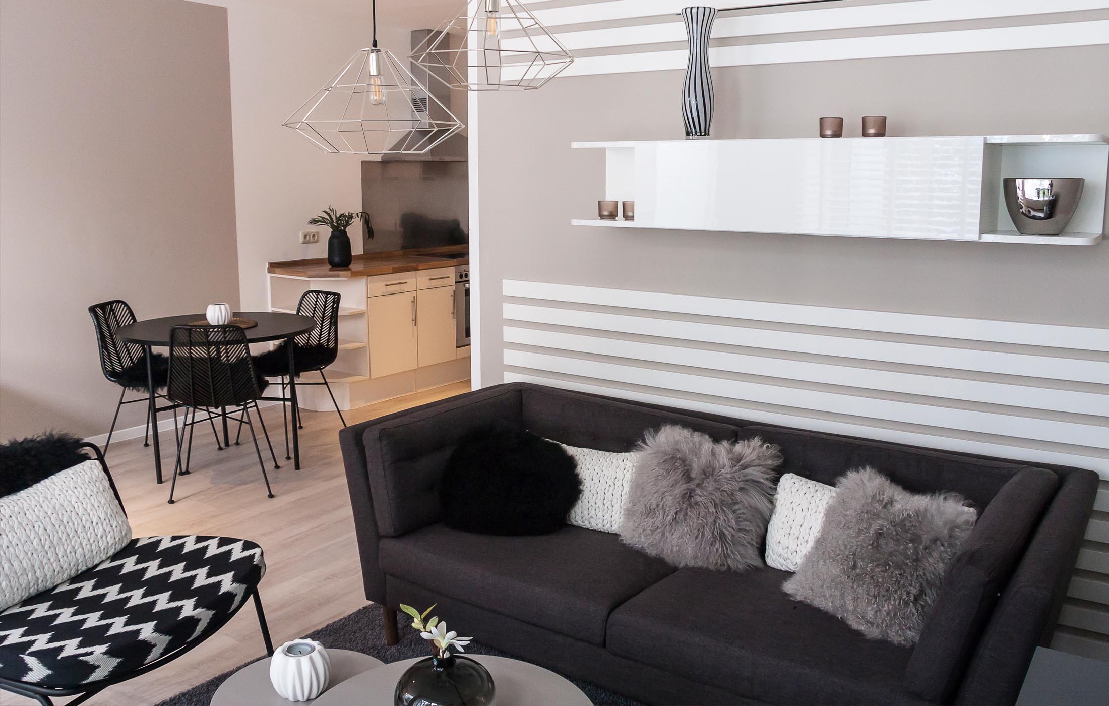 Schwarz-weiße Wandstreifen, schlichte Möbel in Grautönen und moderne Drahtlampen in einem offenen Wohnraum.