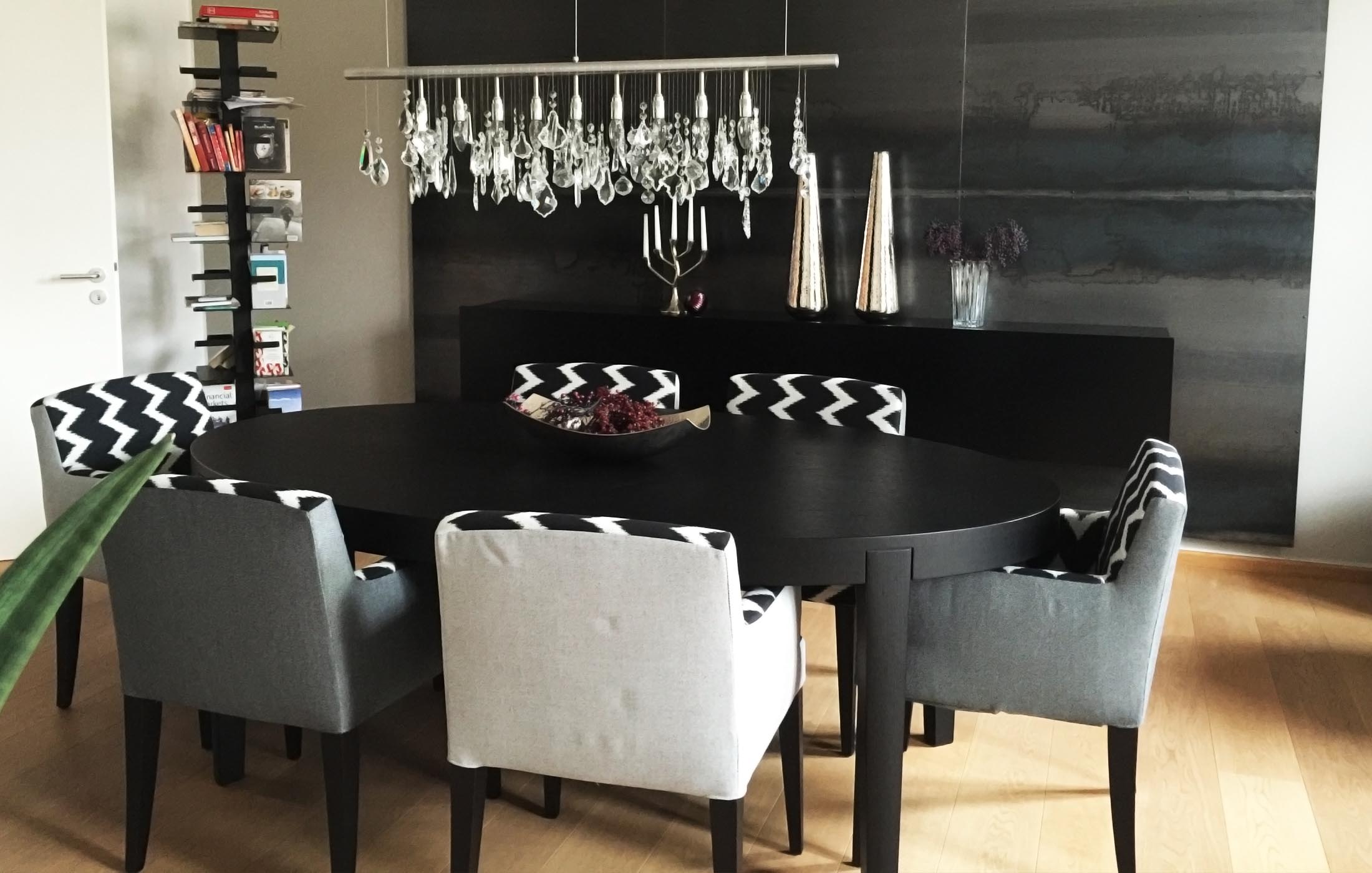 Modern eingerichteter Essbereich mit schwarzem Tisch, gemusterten Polsterstühlen und funkelnder Hängelampe.