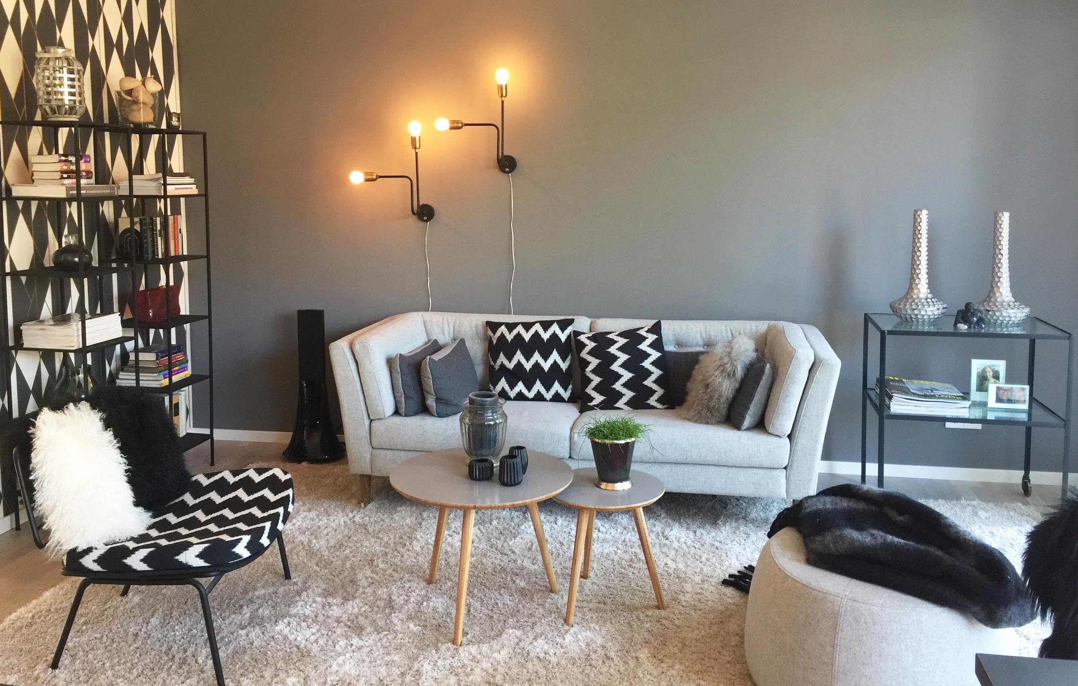 Ein stilvoll eingerichtetes Wohnzimmer mit grauer Couch, gemusterten Kissen, Designerlampen und einem modernen Schwarz-Weiß-Konzept.