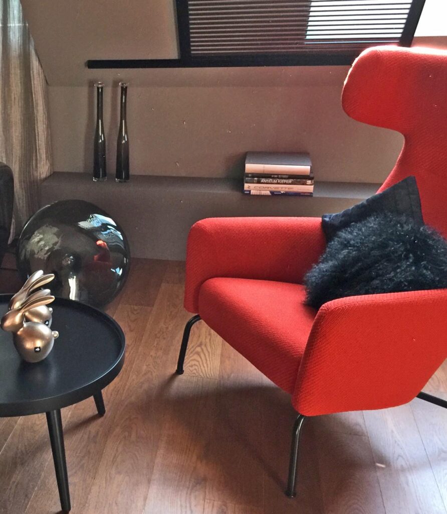 Modern eingerichtete Sitzecke mit rotem Designersessel, schwarzem Kissen und Beistelltisch auf Holzboden.