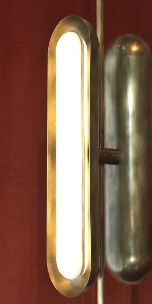 Nahaufnahme einer vertikalen Wandleuchte mit abgerundetem Design in goldener Metallausführung.