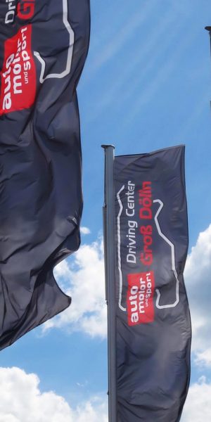 Hohe schwarze Fahnen mit der Aufschrift „Driving Center Groß Dölln“ und „auto motor und sport“ wehen im Wind.