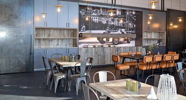 Essbereich mit industriellen Elementen und historischem Motorsport-Bild als Wanddeko.