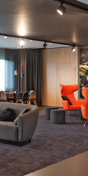 Loungebereich mit roten Sesseln und Sofa vor einer Fototapete der Nürburgring-Rennstrecke.