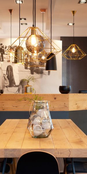 Moderner Empfangsbereich mit Holztheke, Hängelampen und großem historischen Rennsport-Foto.