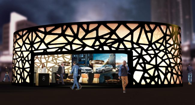 Beleuchteter, runder Messepavillon mit organischem Fassadenmuster und Mercedes-Branding bei Nacht.