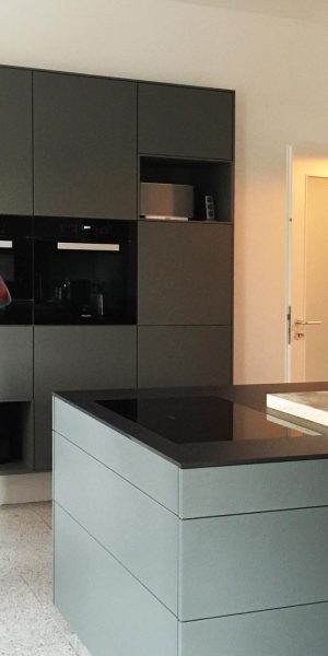 Minimalistische Küche mit ungewöhnlicher Lampe aus roten Glasflaschen über einer Kücheninsel.