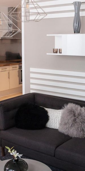 Schwarz-weiße Wandstreifen, schlichte Möbel in Grautönen und moderne Drahtlampen in einem offenen Wohnraum.