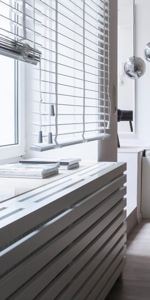 Ein freundlicher Wohnraum mit großen Fenstern, Holzdekor, schwarzer Deko und bunter Wandkunst.