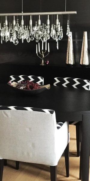 Modern eingerichteter Essbereich mit schwarzem Tisch, gemusterten Polsterstühlen und funkelnder Hängelampe.