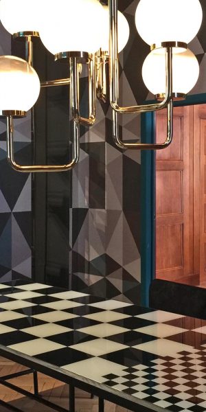 Ein kreatives Esszimmer mit auffälligem schwarz-weißem Schachbrett-Tisch und geometrisch gemusterter Wand.