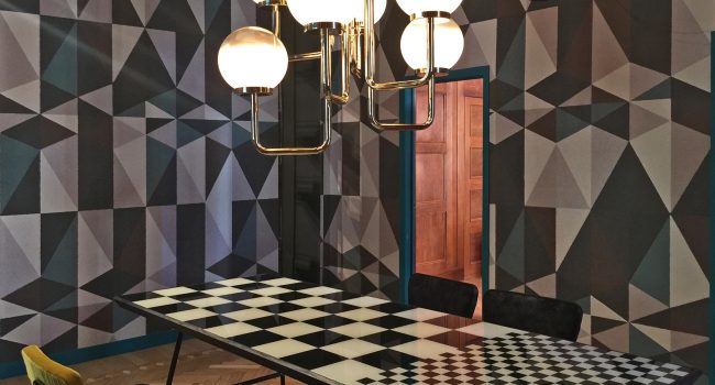 Ein kreatives Esszimmer mit auffälligem schwarz-weißem Schachbrett-Tisch und geometrisch gemusterter Wand.