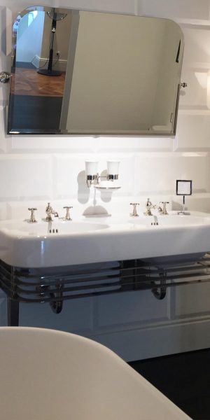 Ein elegantes Bad mit weißem Doppelwaschbecken, Wandlampen, freistehender Wanne und glänzenden Armaturen.