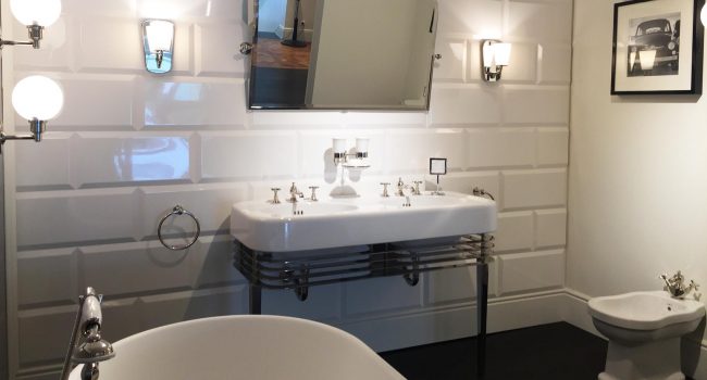 Ein elegantes Bad mit weißem Doppelwaschbecken, Wandlampen, freistehender Wanne und glänzenden Armaturen.